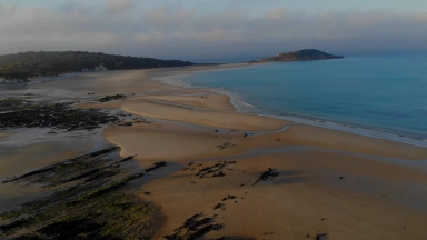 an arial pic of a sandy beach with rocks and blue water with an island in the distance